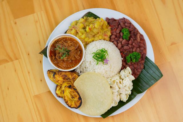 Plato con arroz, frijoles rojos, picadillo, plátano maduro, tortilla, queso y un tazón de carne en salsa.